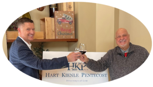 Photo of attorneys Andrew C. Kienle and John H. Pentecost raising wine glasses before firm sign